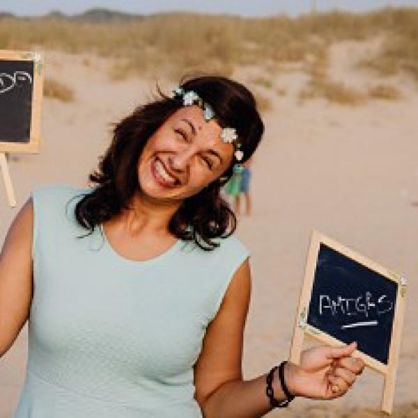 Mulher sorridente numa praia, com uma coroa de flores e quadros de giz nas mãos